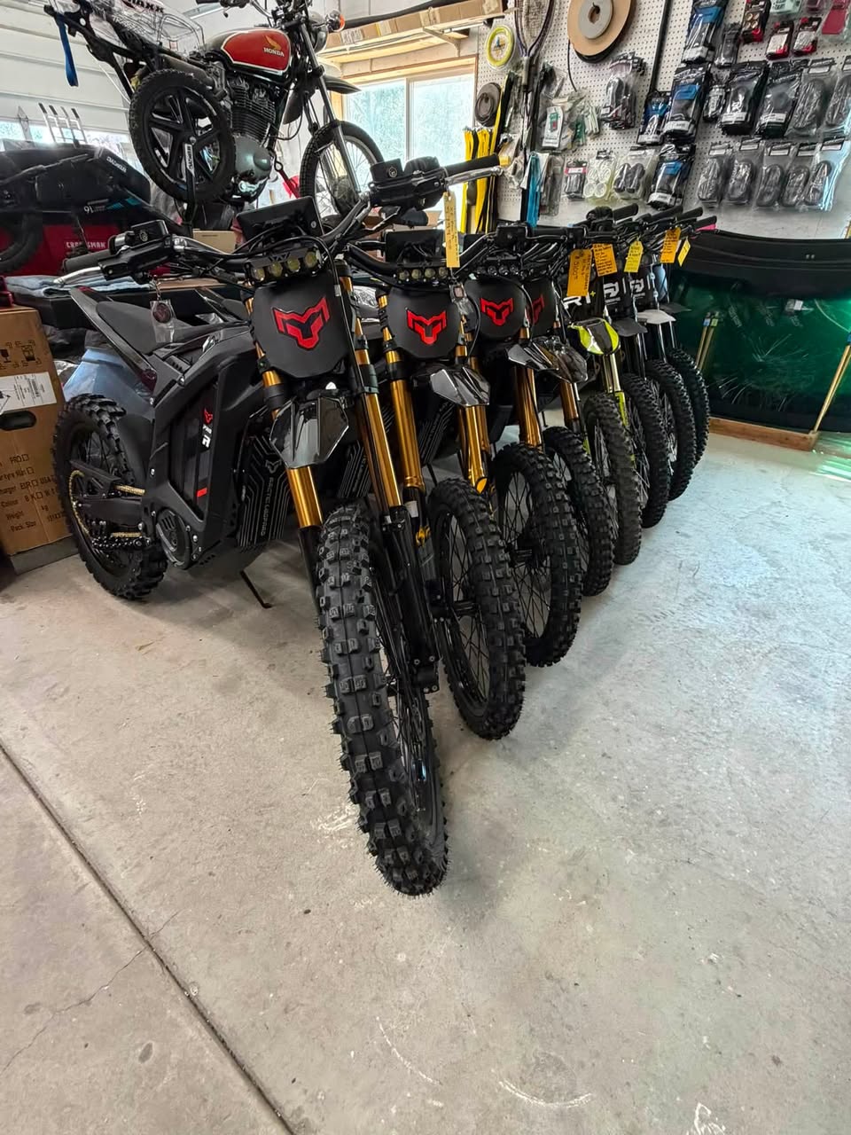 A row of electric dirt bikes with gold inverted forks lined up inside the B&L Specialties shop in Blackfoot, Idaho.